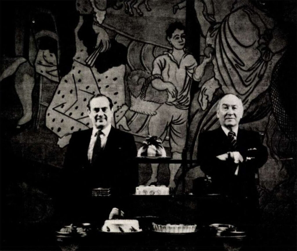 fekete-fehér képen két férfi áll egy falfestmény előtt