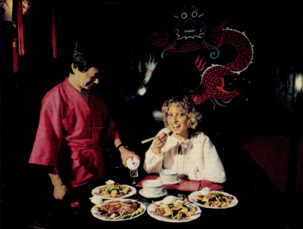kínai étterem, egy nő ül asztalnál, evőpálcikával eszik, egy kínai férfi nézi