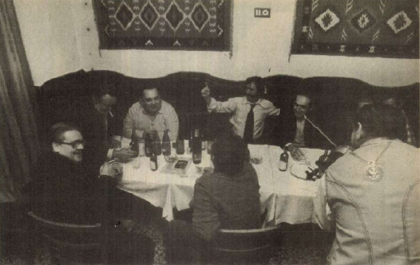 Csukás István barátaival ül egy asztal körül, egyik férfi hegedül