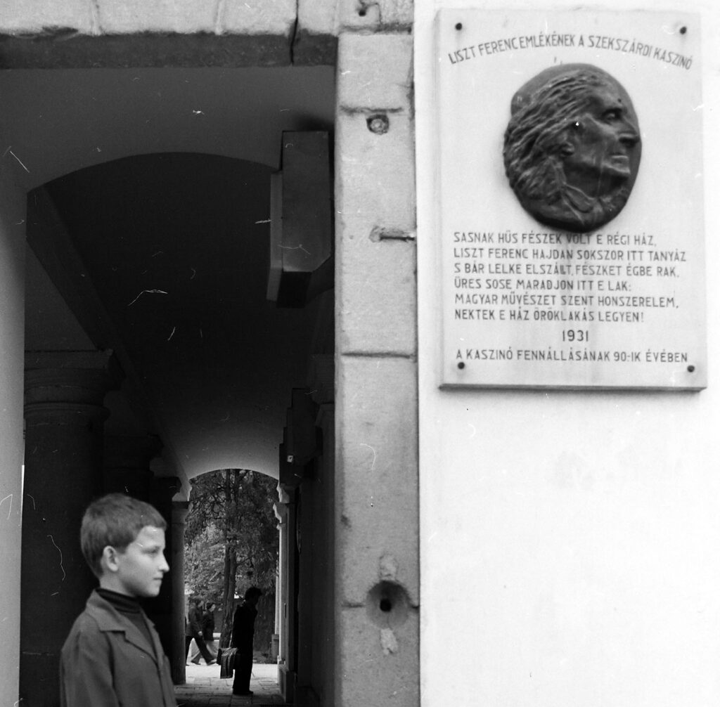 emléktábla egy épületen, ami előtt egy gyerek áll
